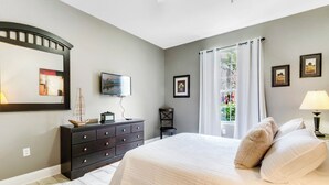 Un dormitorio con cama, cómoda, televisor y ventana con cortinas.