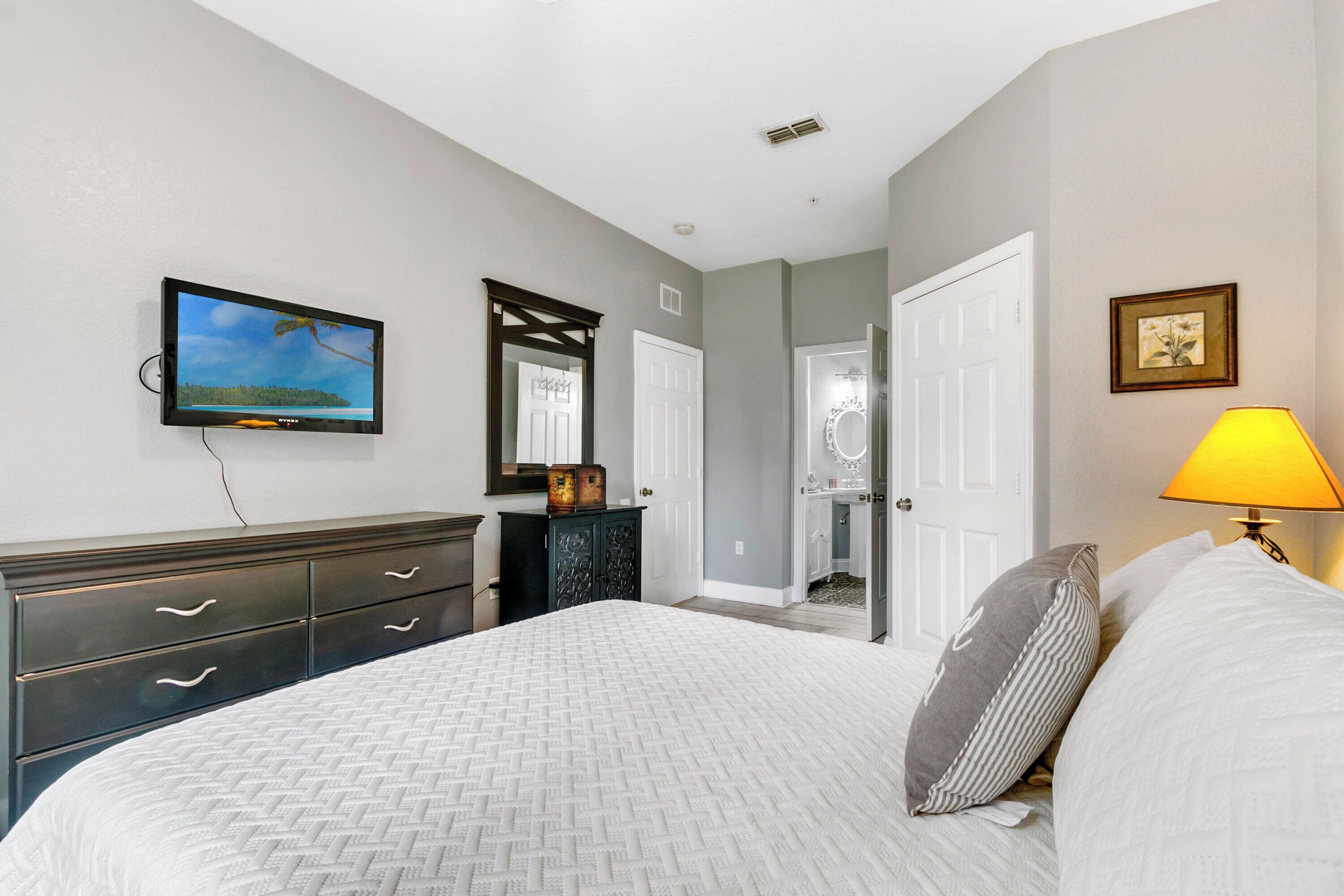 A bedroom with a bed, dresser, television, mirror, and lamp.