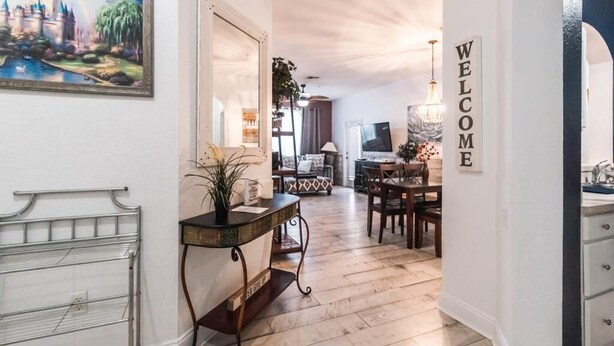 Un pasillo con un cartel que dice 'WELCOME', un comedor con mesa y sillas, un televisor y un cuadro de un castillo.
