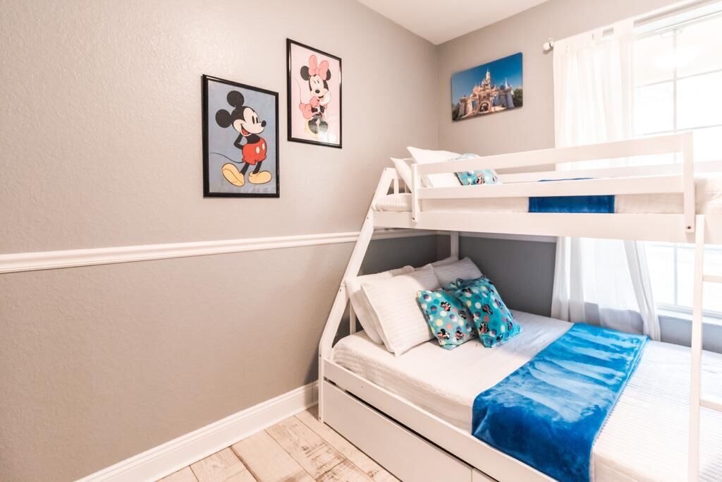 Une chambre avec un lit superposé à la structure blanche, une couverture bleue et des oreillers décorés aux motifs de Mickey Mouse.