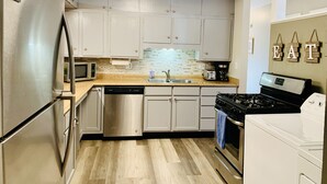 A compact kitchen with stainless steel appliances, white cabinets, and a tiled backsplash.