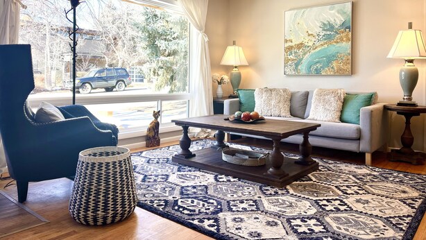 A living room with a sofa, armchair, coffee table, lamps, and a rug.