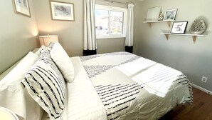 A neatly made bed with striped bedding, a bedside lamp, and a window with curtains.