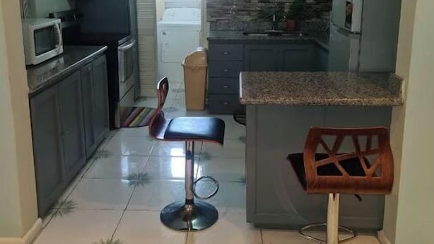 Une cuisine avec des meubles de couleur sombre, un four à micro-ondes, un réfrigérateur et un coin bar avec des tabourets.