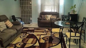 Un salon comprenant un canapé, un fauteuil, une table à manger, des chaises, un ventilateur de plafond et un téléviseur.