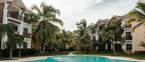 A resort with a swimming pool surrounded by palm trees and multi-story buildings with balconies.