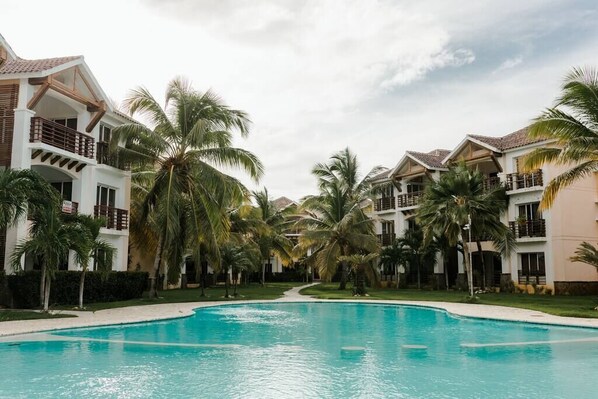 A resort with a swimming pool surrounded by palm trees and multi-story buildings with balconies. - Punta Cana 2 Bedr. up to 6 guests 1 mile to Beach (Punta Cana)