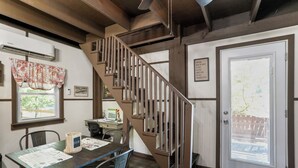 Eine Holztreppe führt zu einer zweiten Etage, einem Essbereich mit Tisch und Stühlen sowie einer Tür mit Blickfenster.