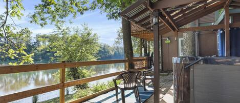 A wooden deck with a view of a lake, two chairs, and a hot tub.