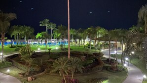A nighttime view of a landscaped area with palm trees, a curved pathway, and distant buildings with lights. - Paradise apartment in beach condo Bay View Grand (Puerto Vallarta)