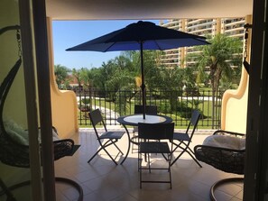 Ein Balkon mit rundem Tisch, vier Stühlen und einem großen Sonnenschirm.