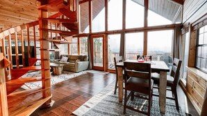 Amplia habitación con escalera de madera, comedor y ventanas grandes que ofrecen vistas.