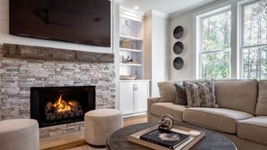 Una sala de estar con chimenea de piedra, un televisor de pantalla plana, un sofá color beige y una mesa de centro con un libro y objetos decorativos.