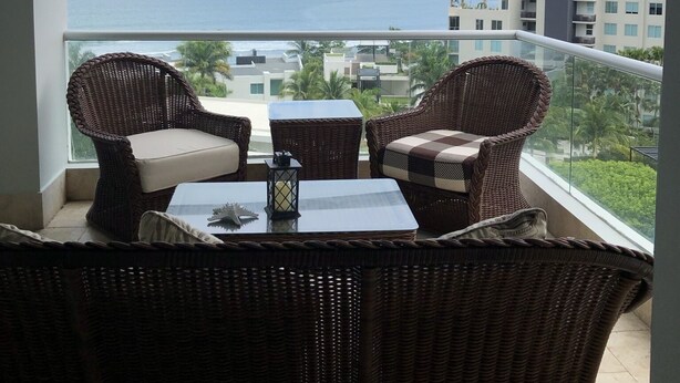 A balcony with wicker furniture and a view of the sea and buildings.