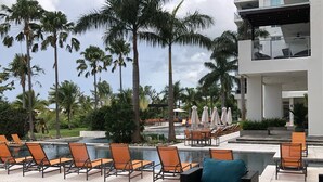 A poolside area with lounge chairs and a seating area, surrounded by palm trees and a modern building.