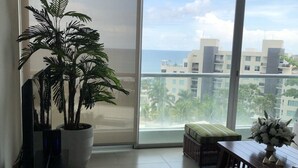 A spacious balcony with a large potted plant, a wicker sofa, and a dining table with a vase of flowers.