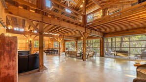 Een ruim interieur met hoge plafonds, houten balken, een eethoek en grote ramen.