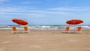 A beach with two orange umbrellas and white chairs facing the ocean.