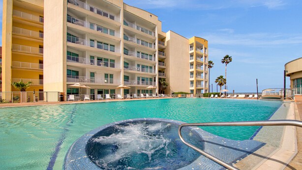 A hotel with a large outdoor swimming pool, multiple balconies, and a hot tub area.