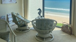 Una habitación con un ventanal grande que da a una playa, dos sillones de mimbre, un adorno con forma de caballito de mar y un cuadro en la pared.