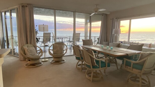 Un comedor con vista al océano al atardecer, que incluye una mesa con sillas y un ventilador de techo.