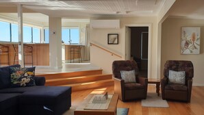 A spacious living area with a sofa, two armchairs, a coffee table, and a staircase leading to an upper floor.