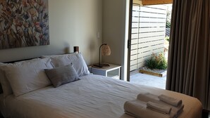 A neatly made bed with white linens and two pillows, a bedside lamp, and a painting on the wall.