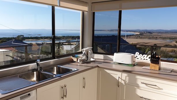 A modern kitchen with a large window offering a view of the sea and distant hills.