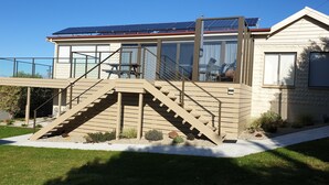A modern house with a glass balcony, a staircase leading to a deck, and a solar panel roof.