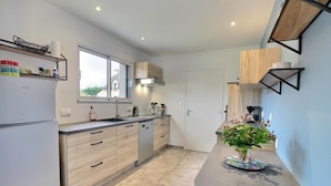 Een moderne keuken met licht houten kastjes, een roestvrijstalen koelkast en een ingebouwde oven. Er is een raam dat natuurlijk licht biedt en een gootsteen met een kraan.