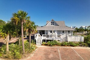 A white two-story house with a balcony, surrounded by palm trees and a brick driveway. - Steps to Beach | Sleeps 12, Game Room & Bay Views in Windmark (Port St Joe)