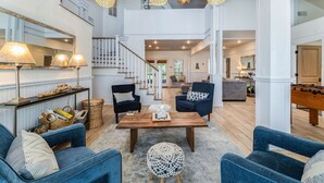 A spacious living room with a high ceiling, a wooden coffee table, blue sofas, and a foosball table. - Steps to Beach | Sleeps 12, Game Room & Bay Views in Windmark | Boat Parking (Port St Joe)