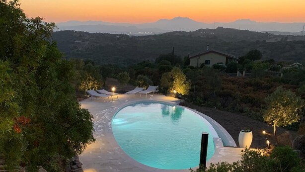 Una piscina con un sendero de piedra que la atraviesa, rodeada de rocas y árboles.