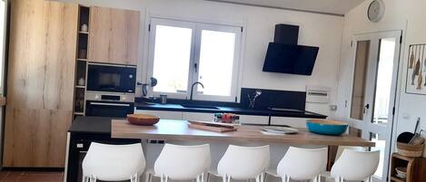 A modern kitchen with a central island, white bar stools, and a built-in oven.