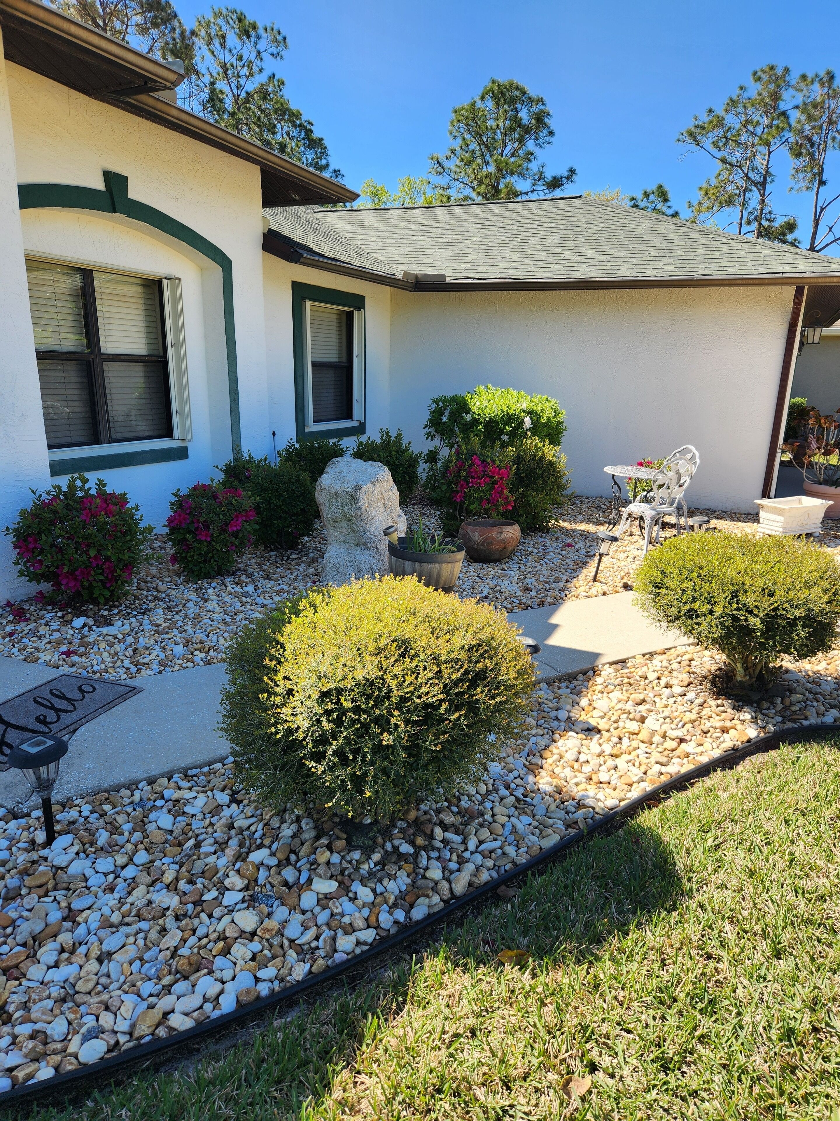 A house with a well-maintained garden featuring a rock sculpture, potted plants, and a pathway.