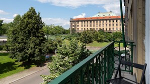 A balcony with a green railing overlooking a street, a large tree, and a building with a red roof in the background. - Luxury spacious apartment in the center (Hlavní mesto Praha)
