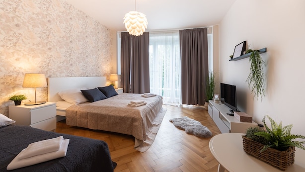 A modern hotel room with a large bed, a bedside table with a lamp, a TV, and a small desk with a plant. - Luxury spacious apartment in the center (Hlavní mesto Praha)