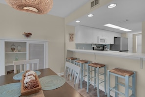 A modern kitchen with white cabinets, a central island, and bar stools. - Sunset & Gulf Views : Updated 2BR : Steps to Beach (Fort Walton Beach)
