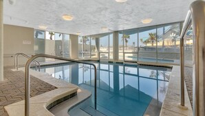 En inomhuspool med väggar av genomskinligt glas, ett kaklat golv och ett tak med infälld belysning.