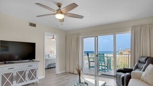 Ett vardagsrum med en TV, ett soffbord i glas, en soffa och en balkong med utsikt över havet.