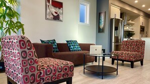 En moderne stue med en brun sofa, mønstrede lænestole, et glas sofabord og en bærbar computer.