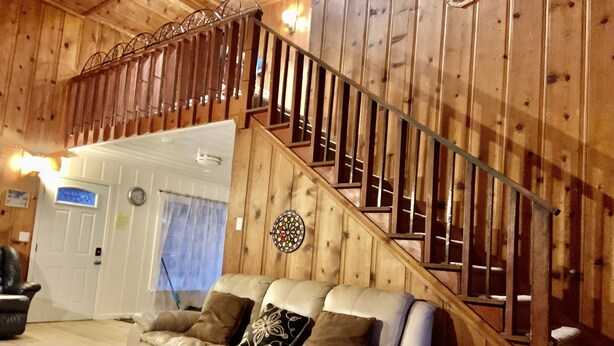 Ein Holzinnenraum mit einer Treppe, einem beigefarbenen Ledersofa und einem Dartboard an der Wand.