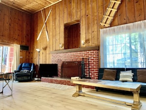 A rustic wooden interior with a brick fireplace, a leather armchair, a sofa, and a wooden coffee table.