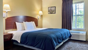Ein Hotelzimmer mit einem hölzernen Kopfteil, einem großen Bett mit blauer Bettwäsche, zwei Nachttischlampen, einem Fenster mit Vorhängen und einem Wandbild.