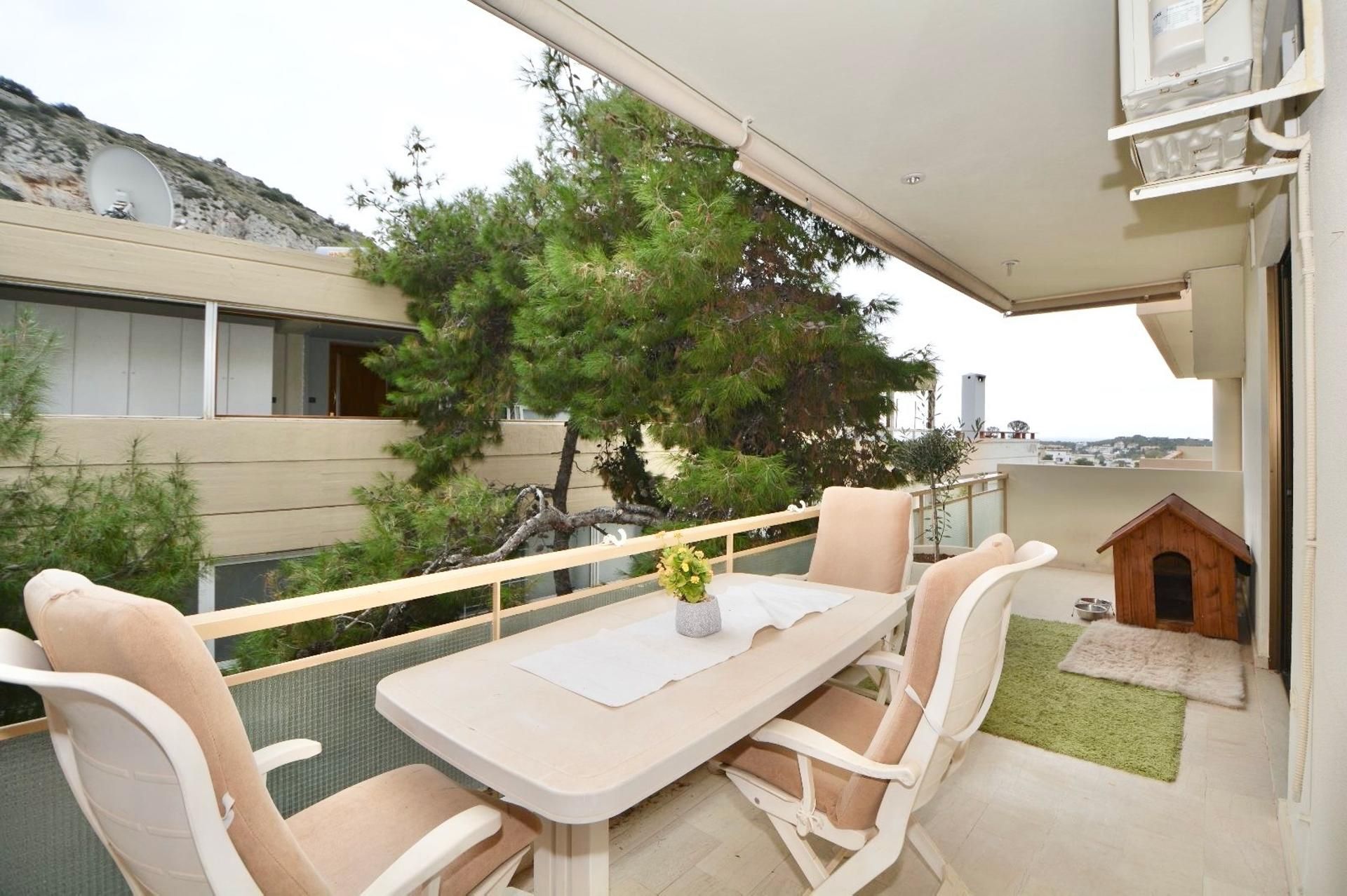 A balcony with a table and chairs, a small dog house, and a view of the surrounding area.