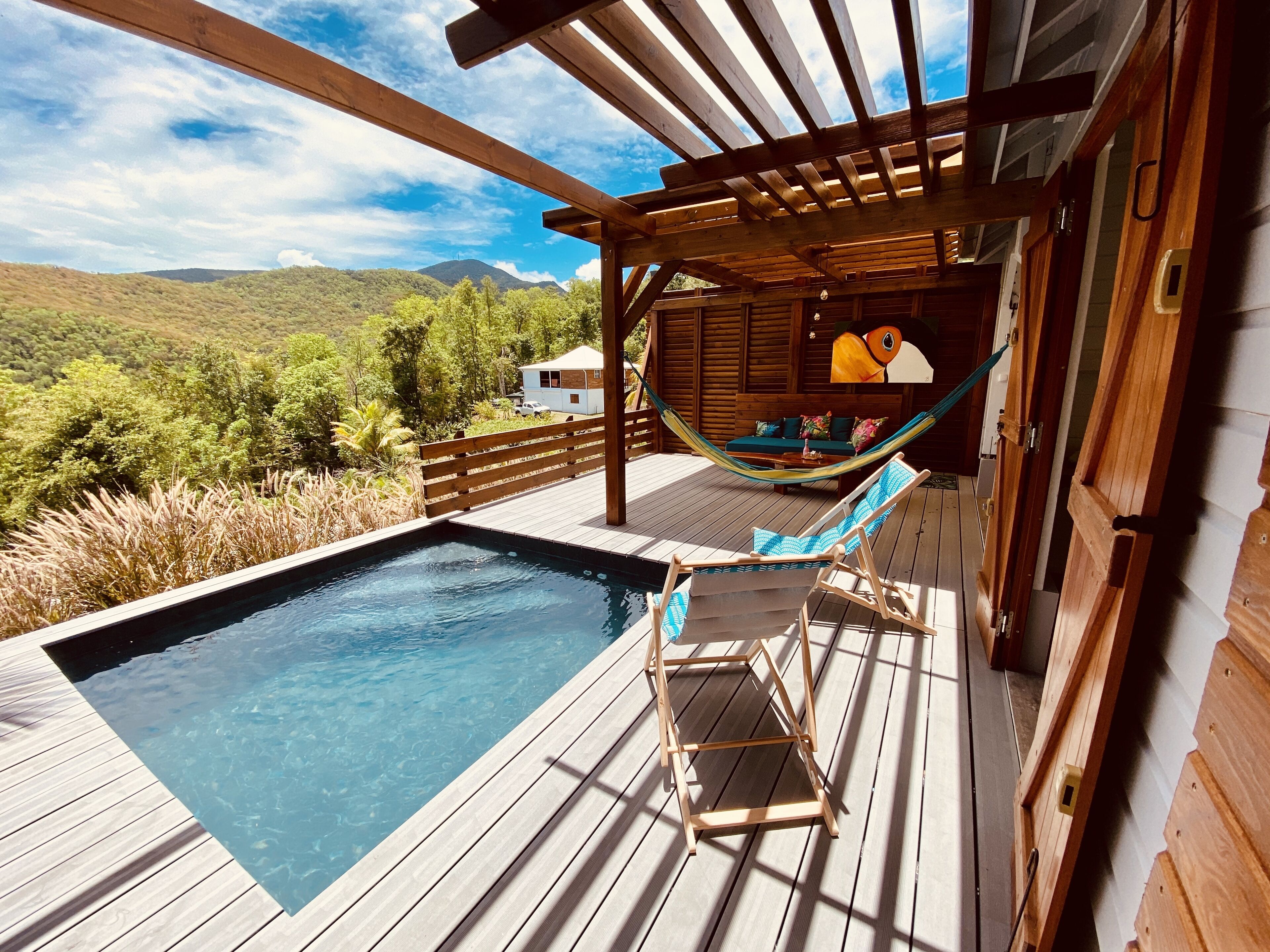 A wooden deck with a swimming pool, a hammock, and a view of the mountains.
