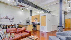 Un espacio habitable moderno con un sofá de cuero, un sillón gris, una mesa de centro de madera y una cocina con armarios y electrodomésticos de madera.