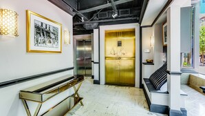 Un interior moderno con un banco, una fotografía enmarcada y una puerta de ascensor dorada.