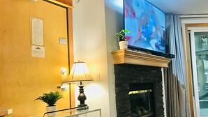 Een kamer met een open haard, een televisie erboven, een lamp en een klein plantje op de schoorsteenmantel.