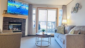 Een woonkamer met een stenen open haard, een flatscreen televisie, een bank, een ronde salontafel en een balkon met tuinmeubilair.